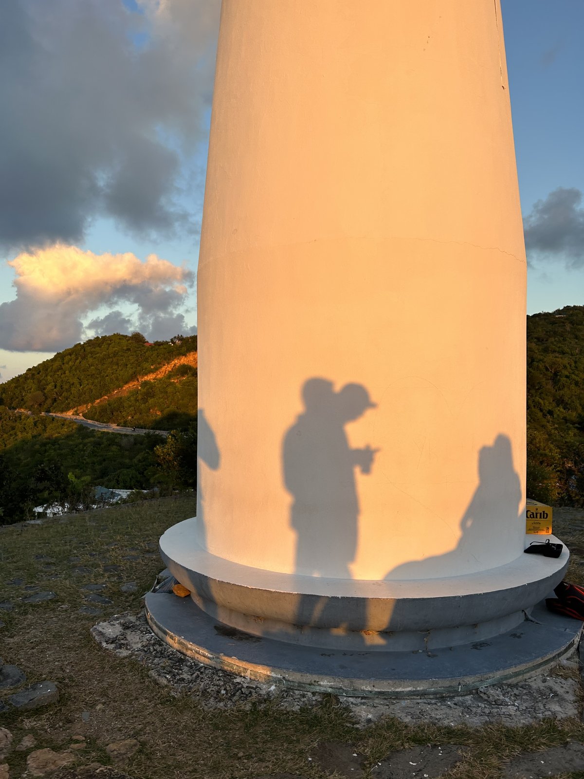 Le phare de Saint-Barthélemy au coucher du soleil, des ombres projetées sur la tour, collines et ciel doré.